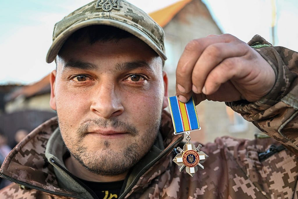 A man dressed in fatigues holds up a medal he earned during Russia’s war in Ukraine.