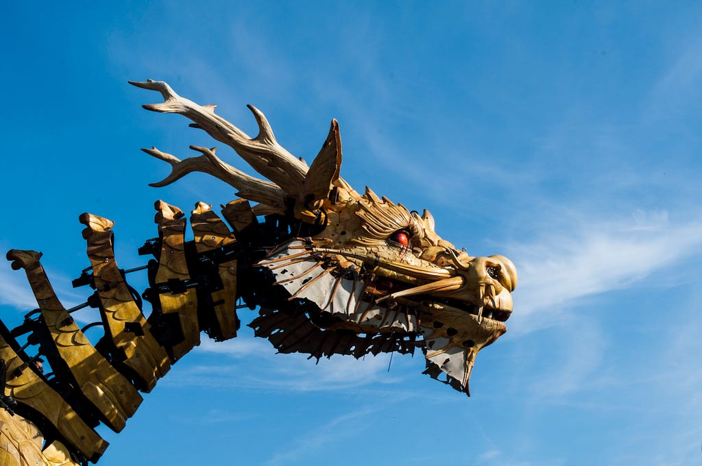 An art installation of a dragon’s head and neck against a blue sky with wispy clouds