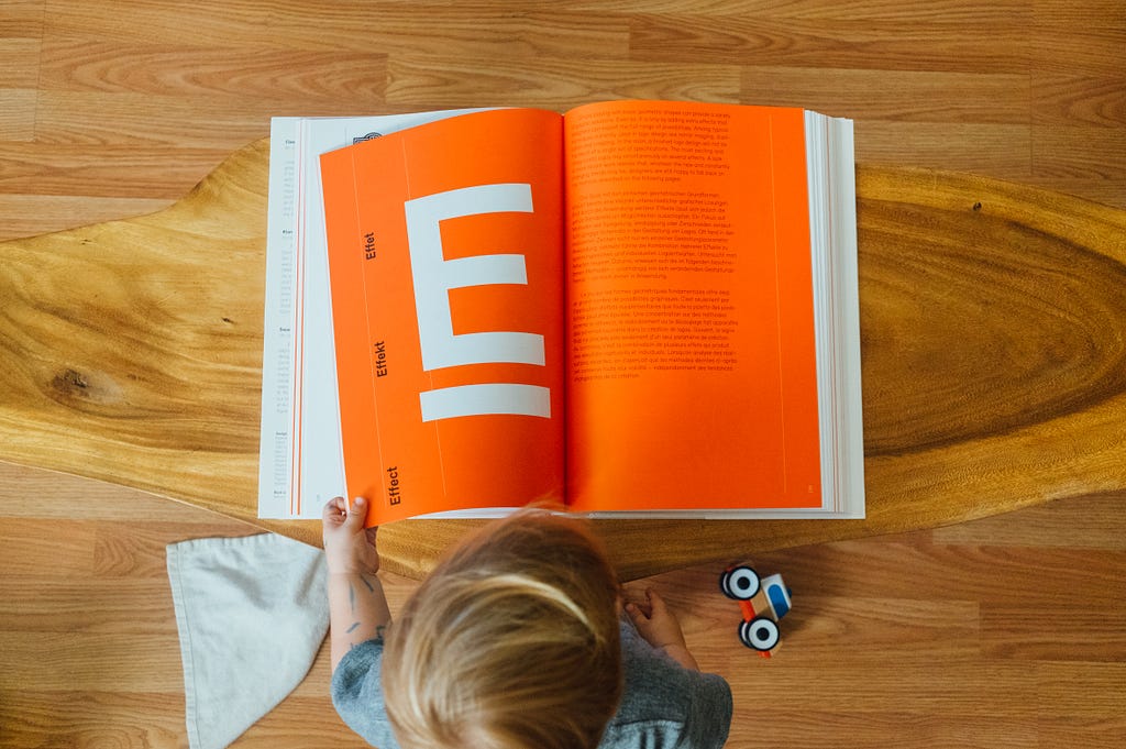 Child looking at a book with orange pages with the letter E on the left page