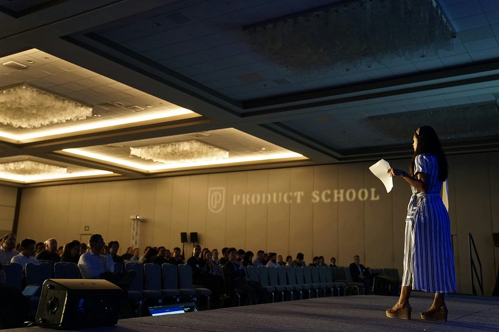 A person on a stage for Product School giving a seminar looking out over an audience