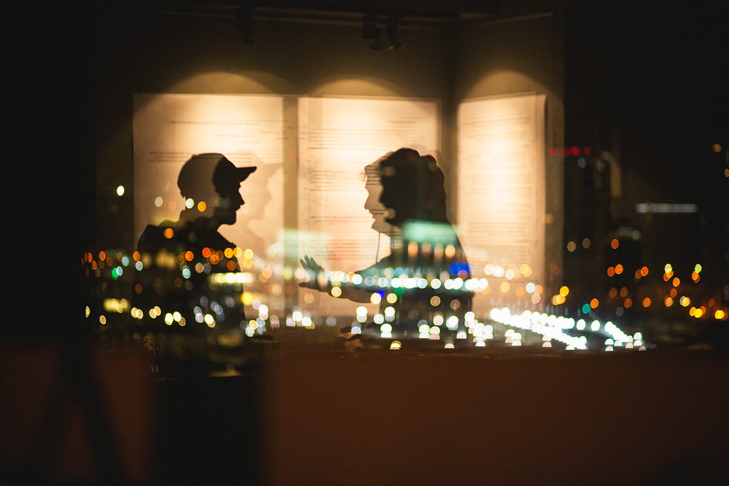 two shadows on a windowpane with city lights in background