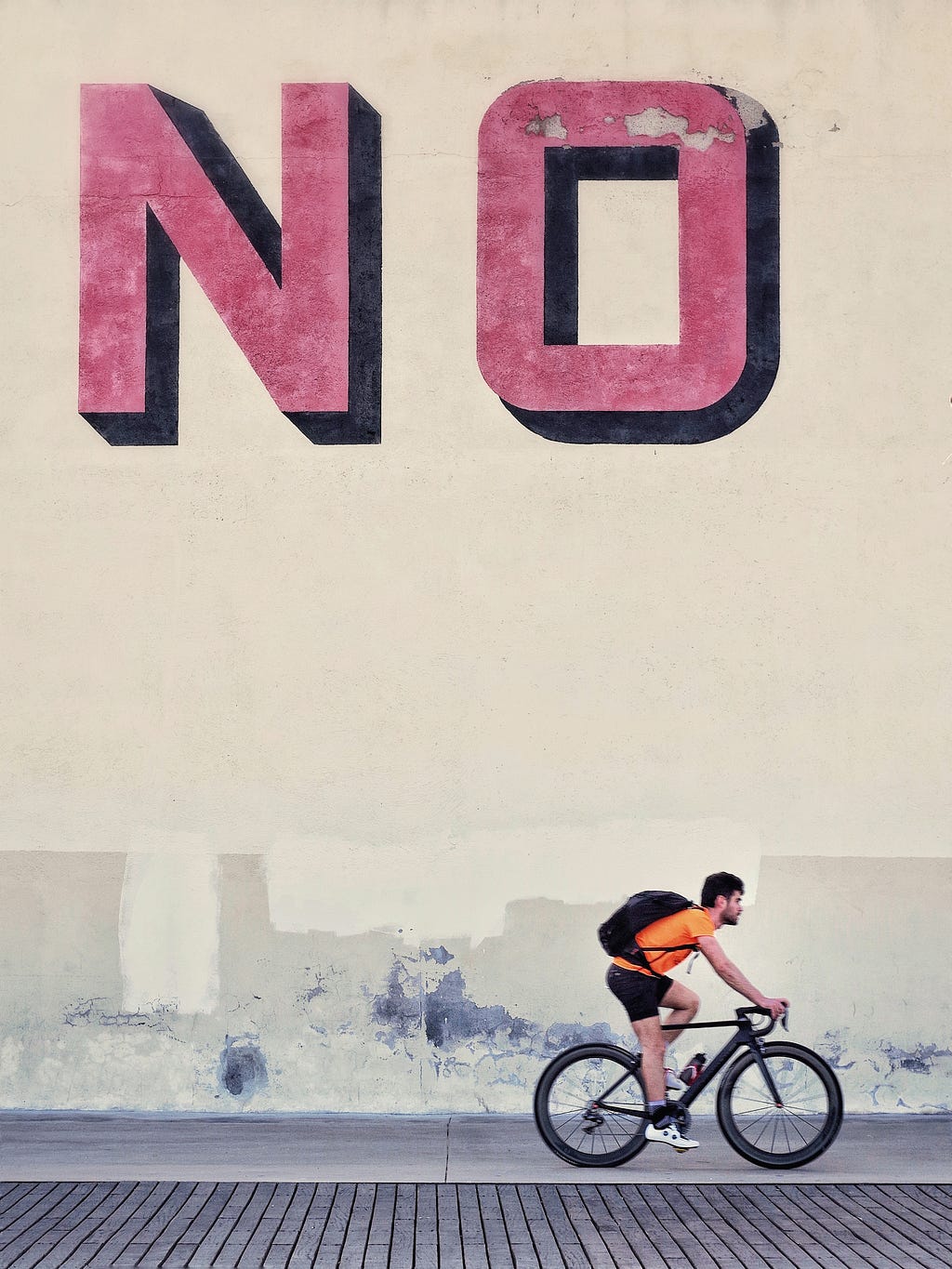 A picture with “NO” written on a wall while a biker rides ahead.