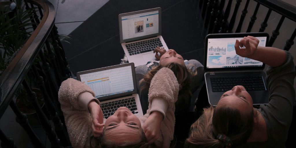 Three girls listening to headphones using laptops