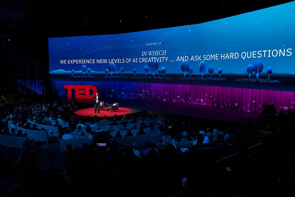 TED stage, a large wrap-around screen behind the speaker Chris Anderson reads: Session 10: In Which We Experience New Levels of AI Creativity … and Ask Some Hard Questions