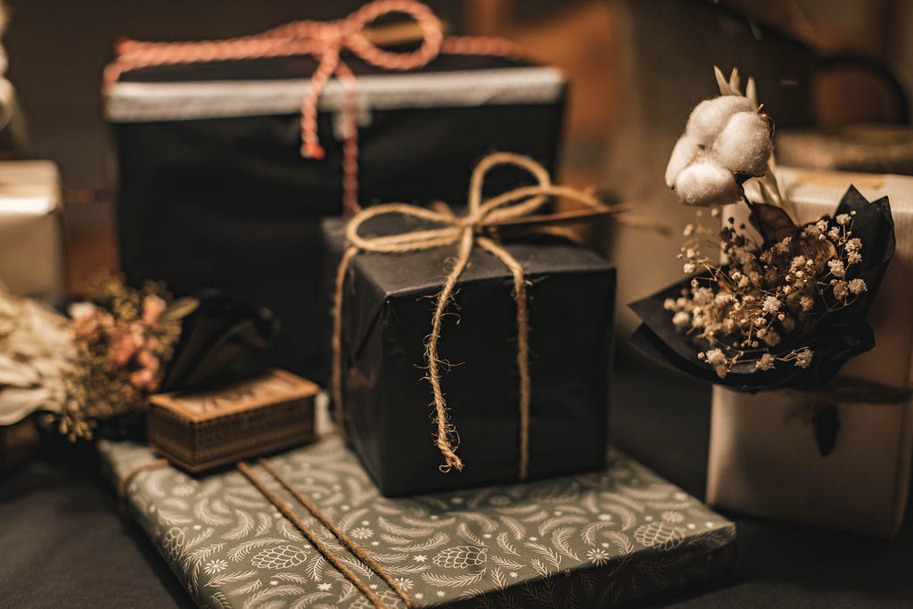 A few presents wrapped in black with a twine bow tied on top sit on top of a black table.
