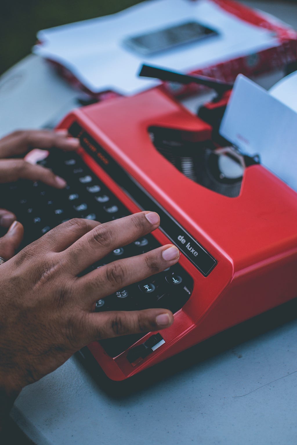 Black hands type on a red typewriter.
