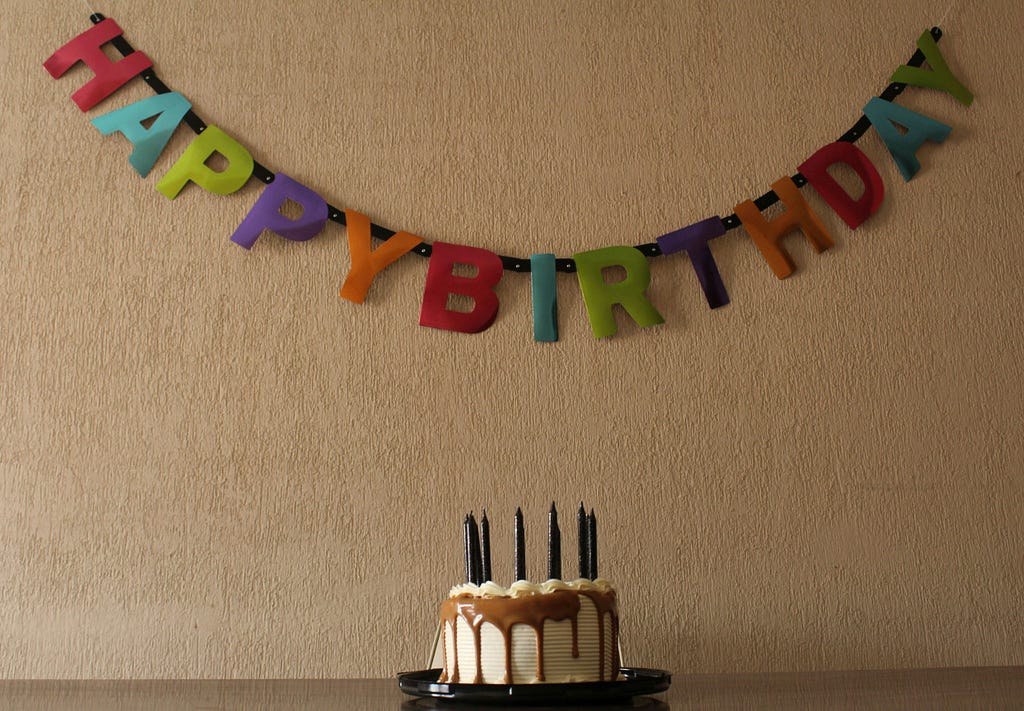 Rainbow colored letters for happy birthday strung on the wall behind a cake with candles.