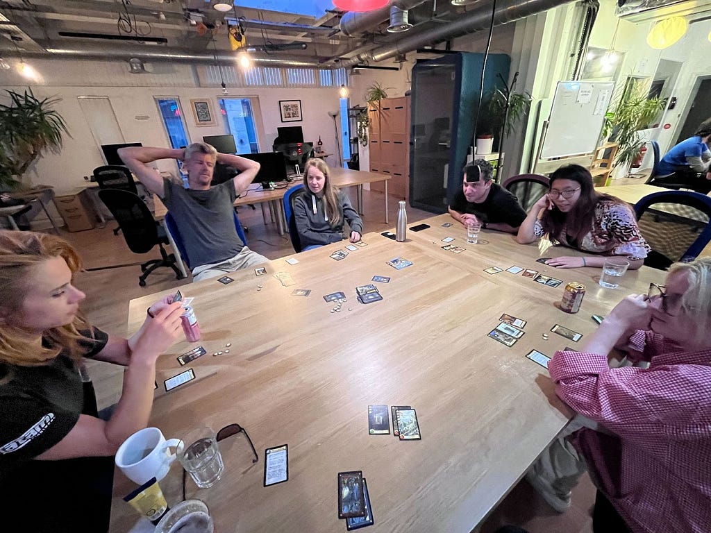 Men and women sitting around a large table in an office playing a card based game