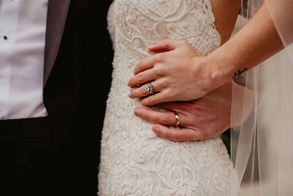 Close-up of a couple holding hands on their wedding day, showcasing intricate wedding rings and a sparkling engagement ring in Toronto.