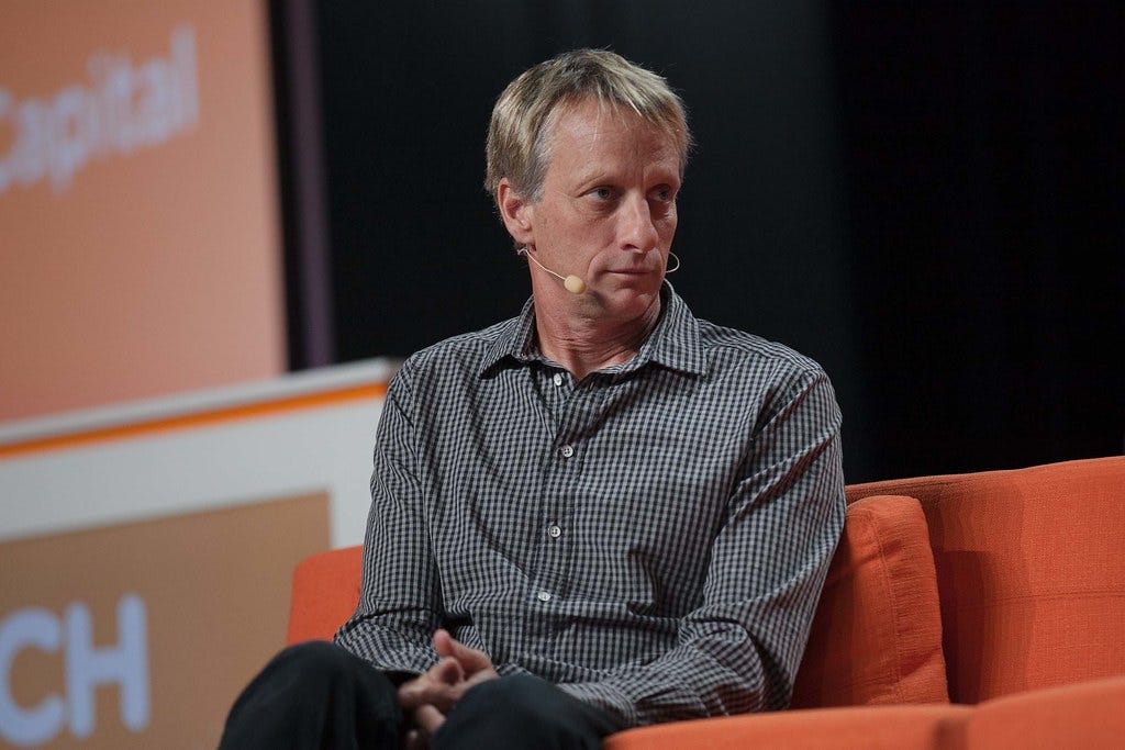 Tony Hawk sitting on a couch in a dress shirt, fitted with a no-hands microphone.