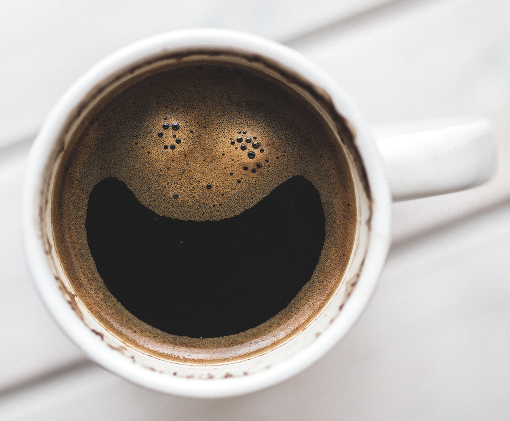 A cup of coffee with surface bubbles that look like a smiley face