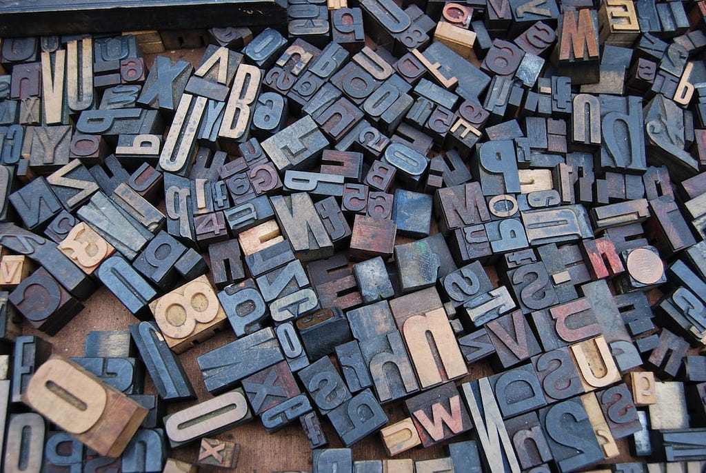 Typesetting letters and numbers of various sizes randomly strewn around in a wooden box.