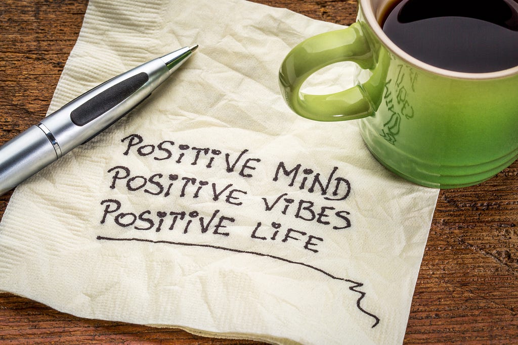 Overcoming adverisity—"positive mind,  positive vibes, positive life"— motivational handwriting on a napkin with a cup of coffee.