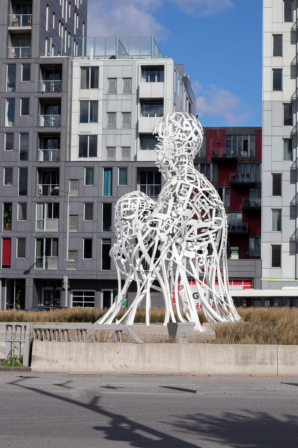 A large white sculpture with a backdrop of skyscrapers. The sculptur is a human figure made of white wires.