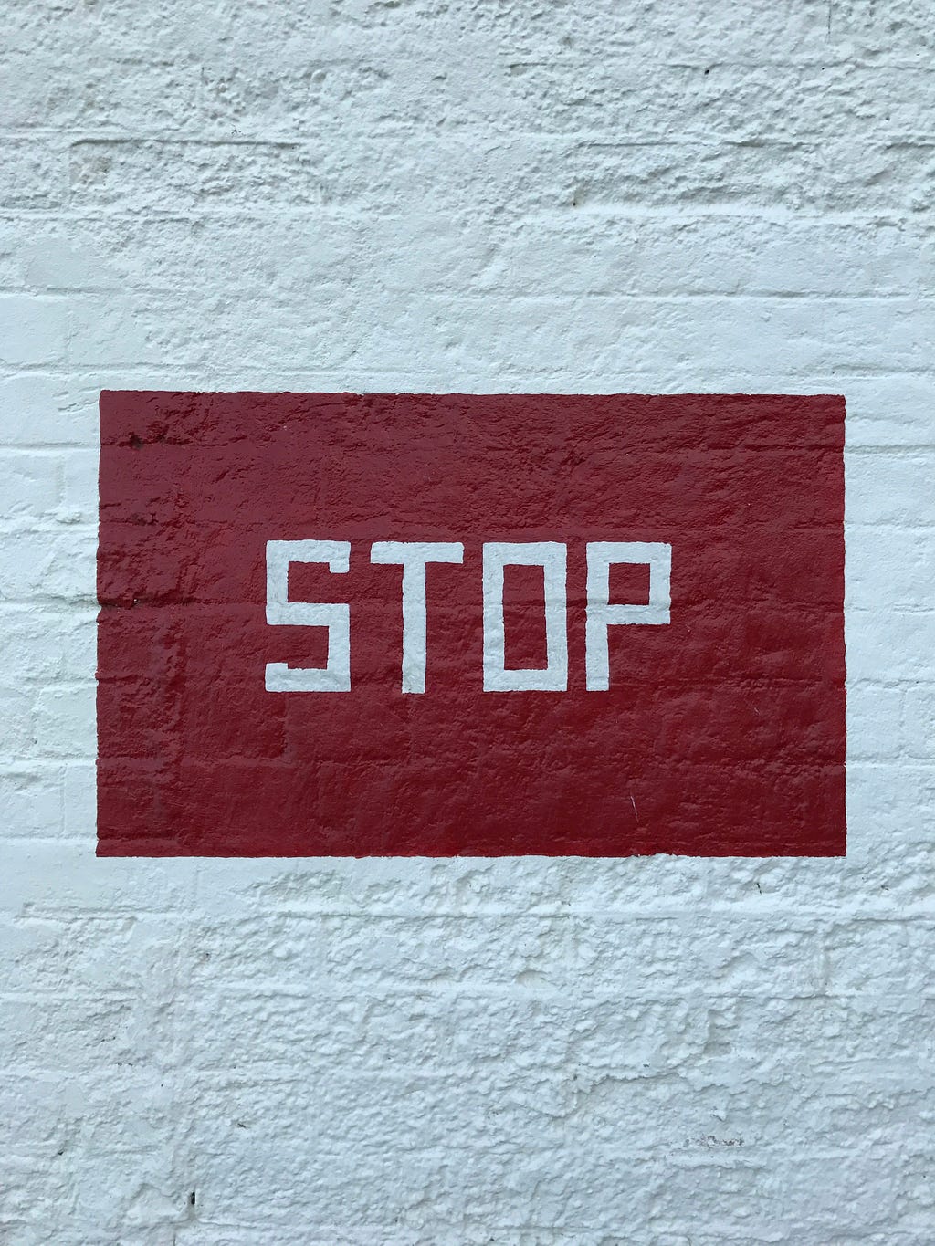 painted stop sign on a white brick wall