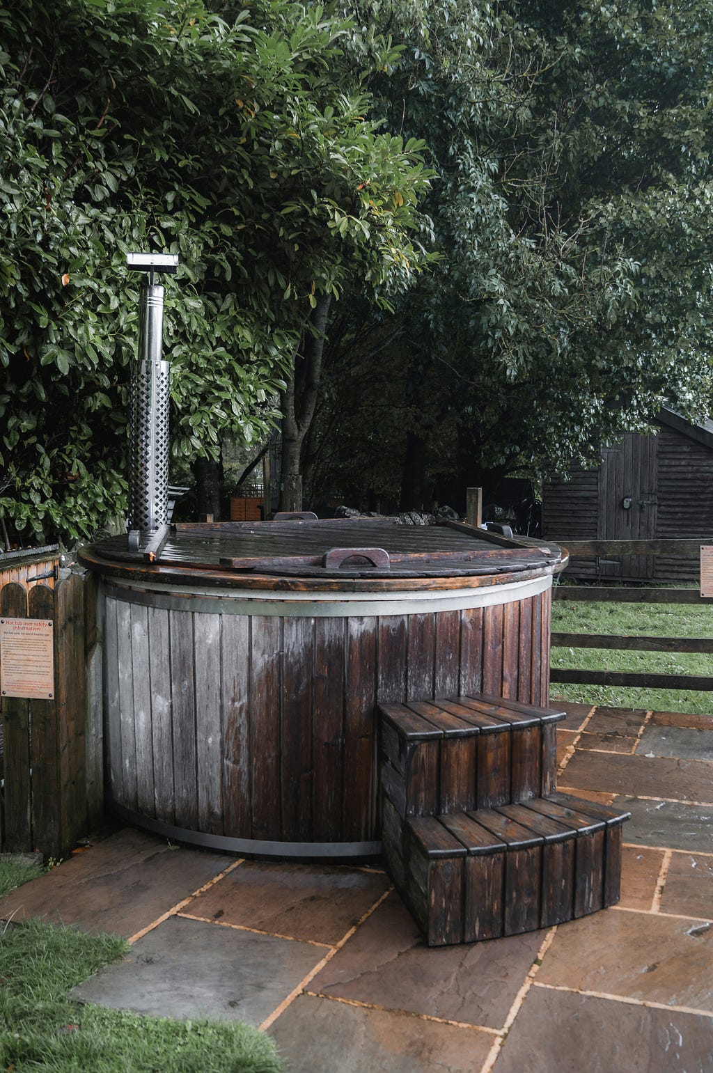 An outdoor wooden hot tub with trees and grass on the background.