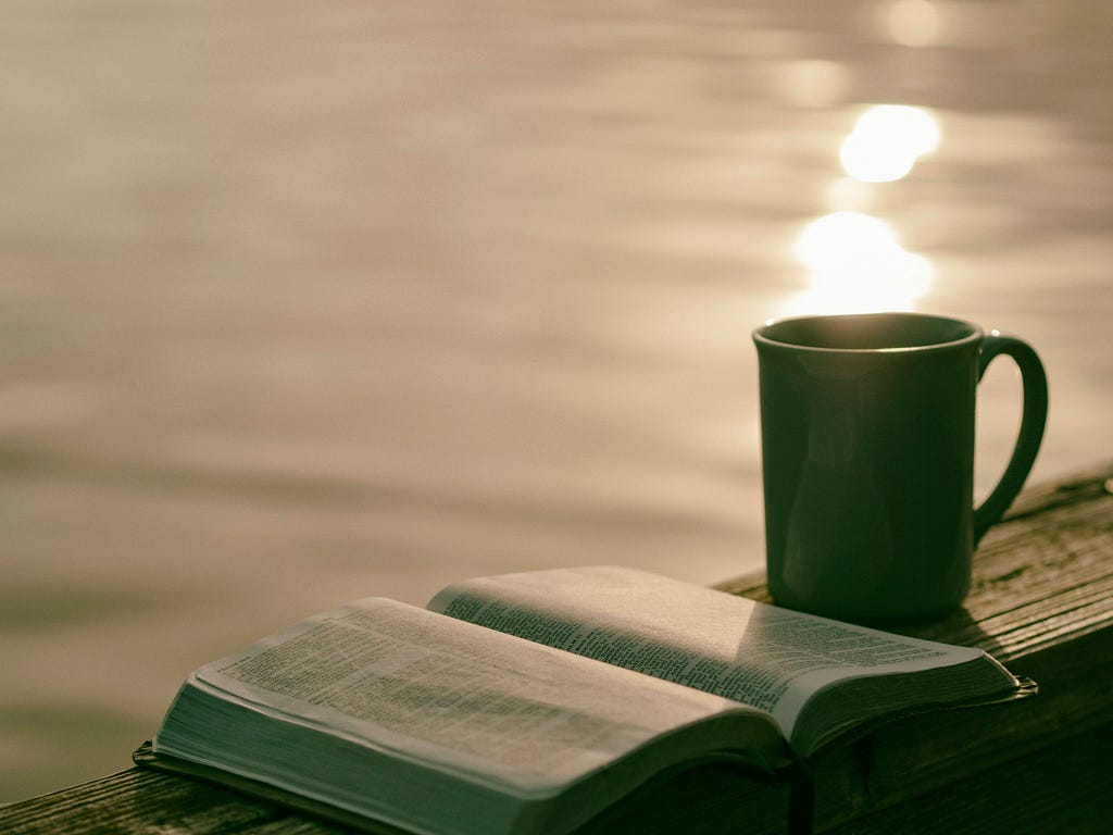 Image of coffee mug next to an open book on a pier over a body of water