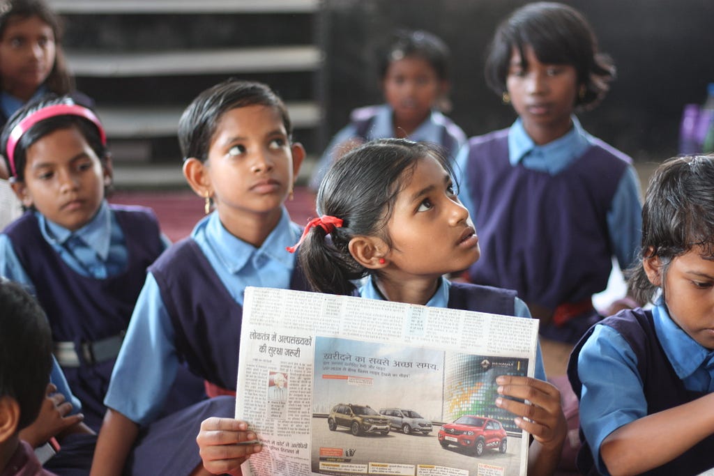 A school girl reading a Hindi newspaper and looking up.