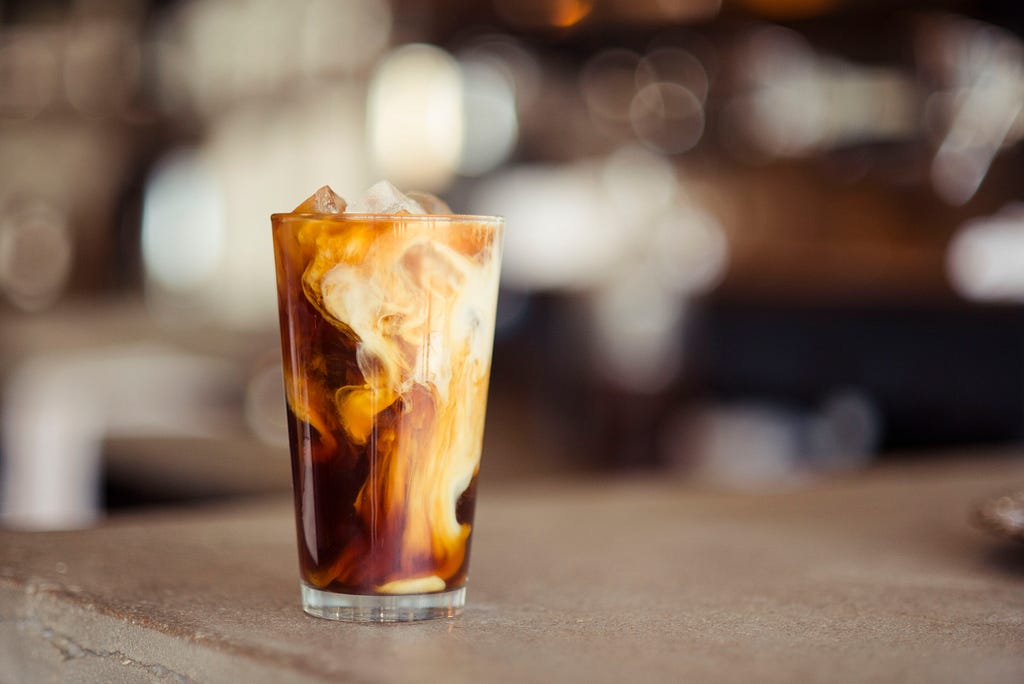 A cup of iced coffee sits on a table with a blurred background.
