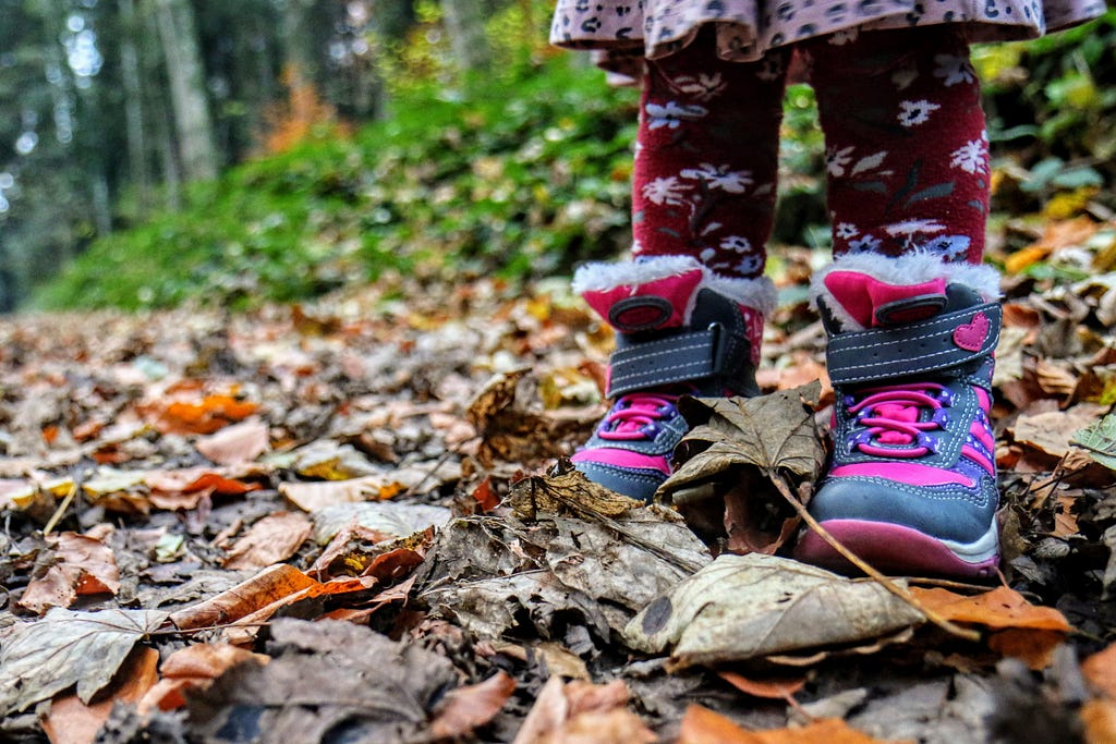 A child standing on a pile of crushed leaves in a pair of winter boots.