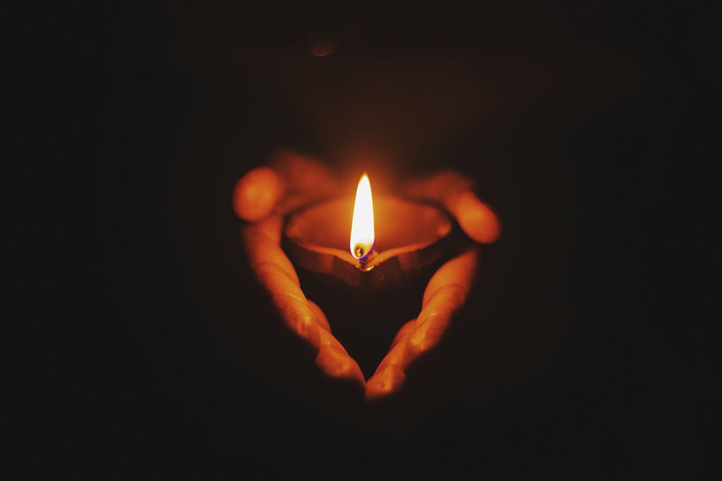 A pair of hands hold a small candle in the darkness.