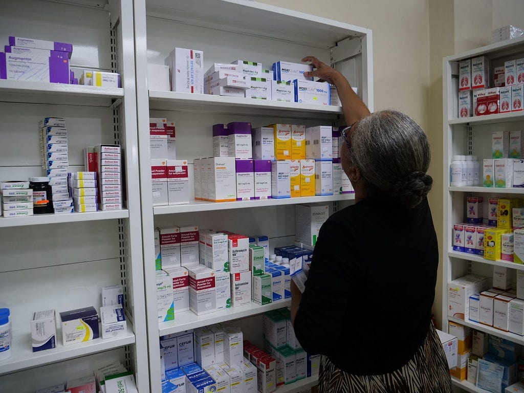 A pharmacist staff member replaces medicines on a shelf.