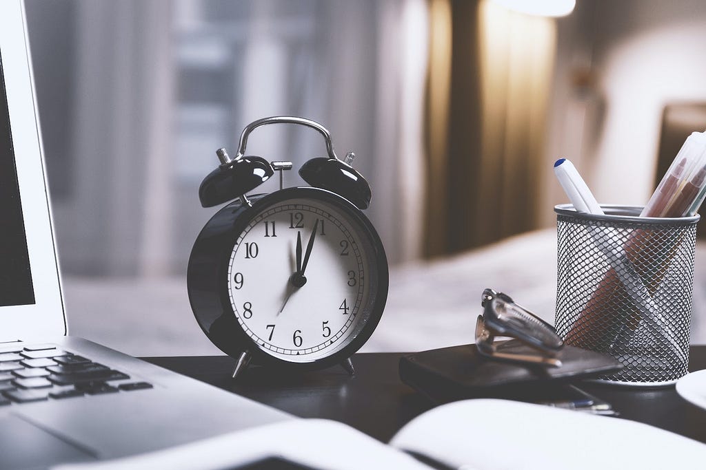 A laptop, a black alarm clock and a pen holder on a black desk