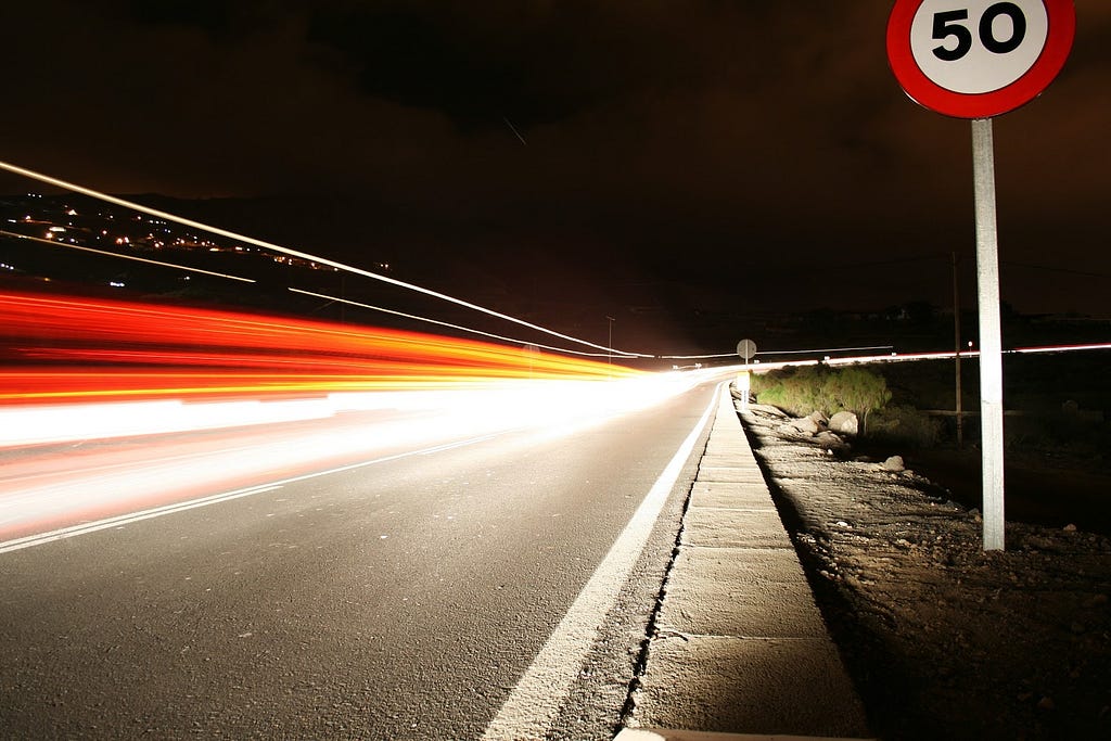 black road with orange and white flash of light along the side and red and white circular sign with “50” written inside it