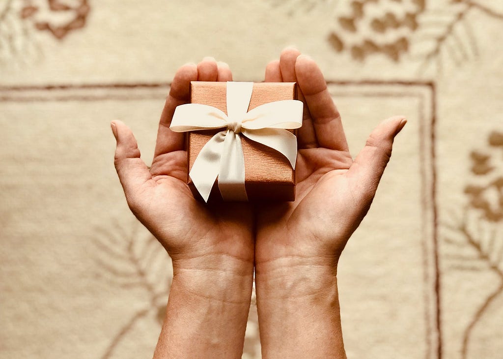 Two hands holding a small, wrapped gift box
