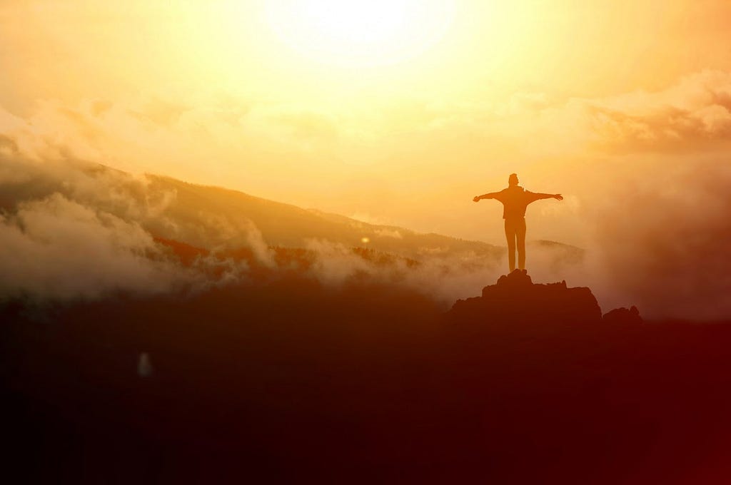 Photo of someone standing on top of a mountain with arms stretched out from their sides.