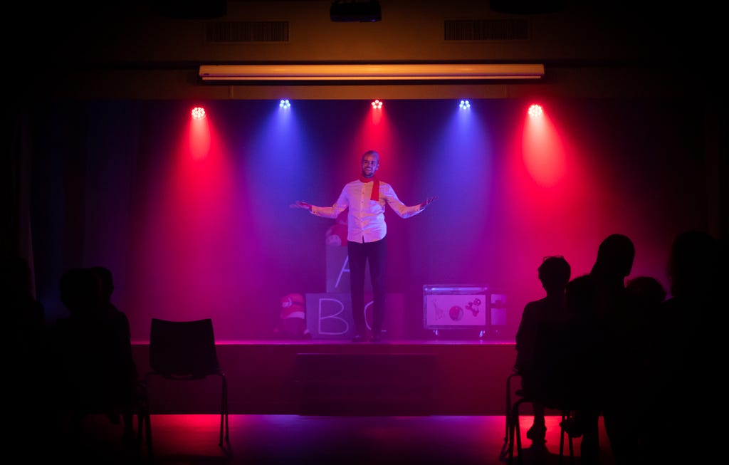 A man on stage with arms spread, lit by alternative red and blue spotlights