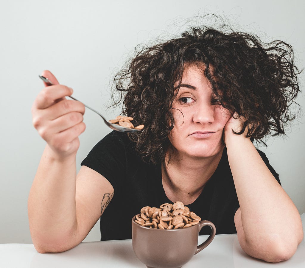 A woman in a black shirt looking hungrily to a spoon in her hand full of small biscuts