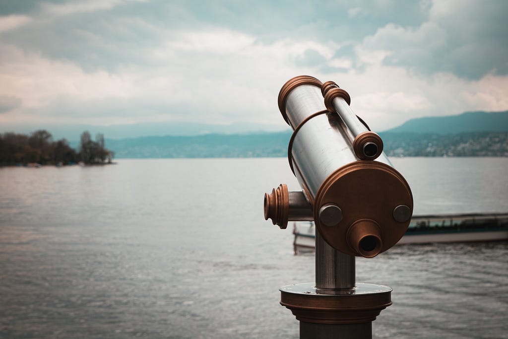 A telescope pointed towards a calm lake on an overcast day