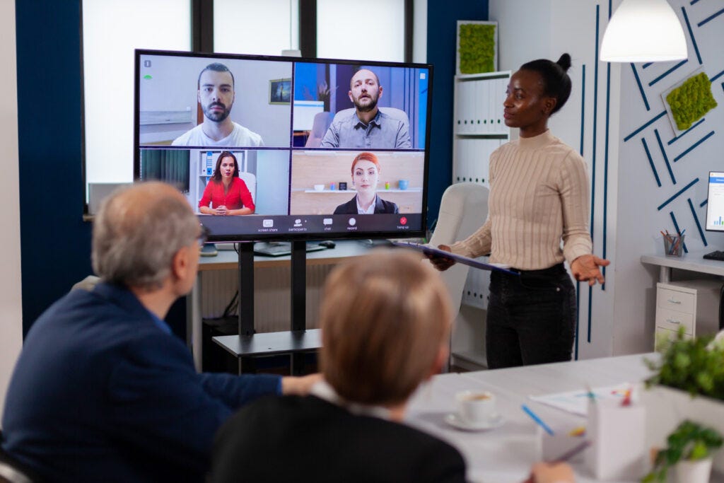 black-manager-woman-talking-with-remotely-colleagues-video-call-tv-screen-presenting-new-business-partners — RumboMag — A virtual workplace is a work environment where employees do not physically come into an office or central location to perform their job duties