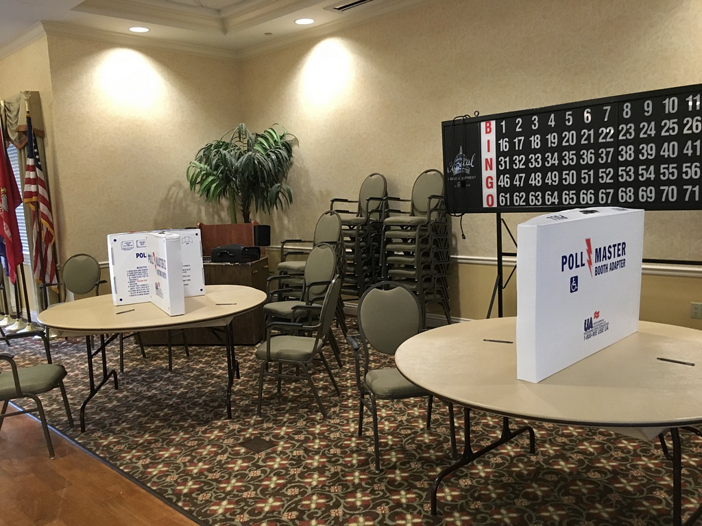 Large room with 2 round tables and boxes arranged to make privacy booths for voting