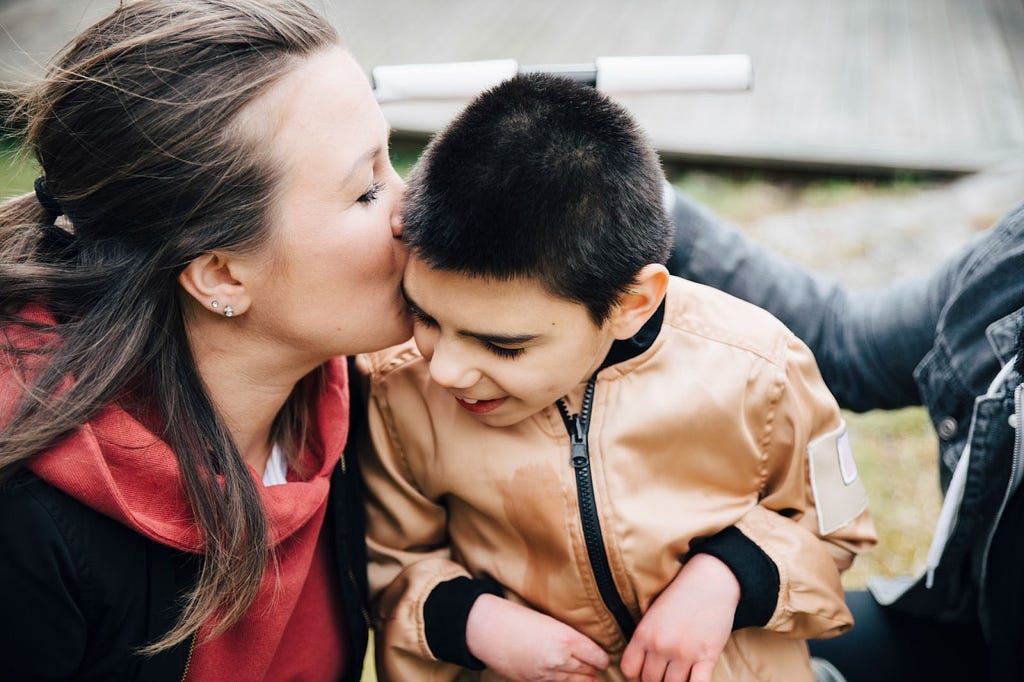 Mother kissing son in a wheelchair — benefits of genetic testing for neuromuscular conditions