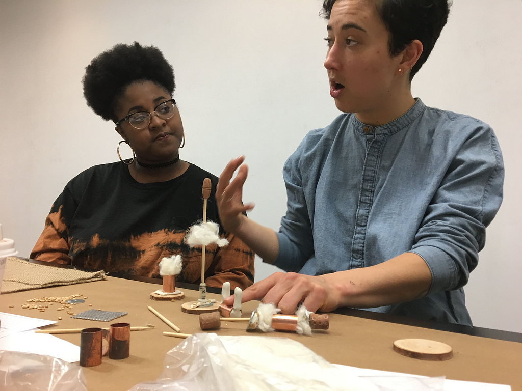 Image from workshop: two students at a table presentng crafts from a future world.