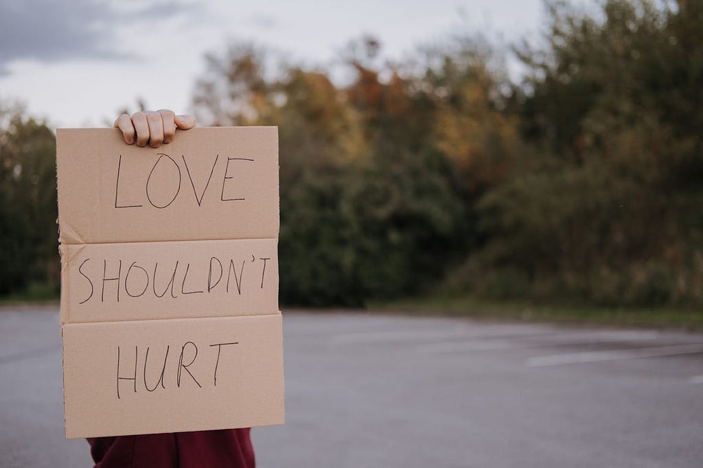 Person with sign stating “love shouldn’t hurt”
