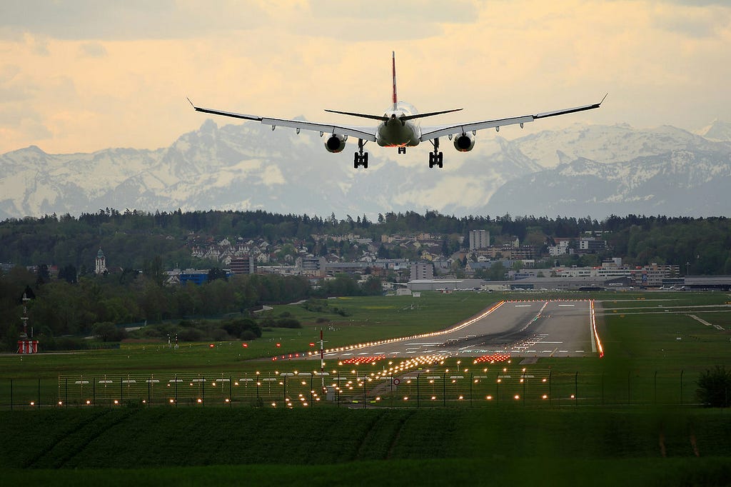 A plane coming in to land, viewed from behind, with a clear runway and distant mountains in the shot