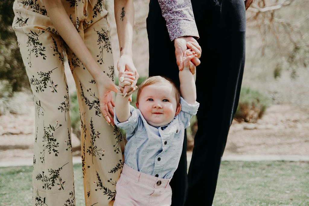 A young child holding the hands of her parents