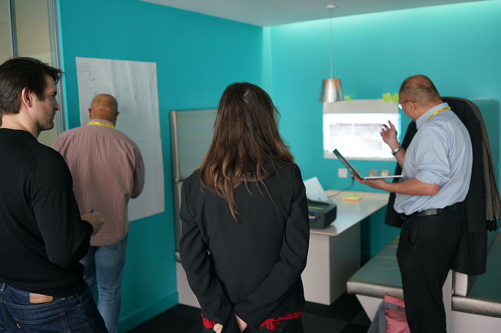 A group of people standing up and using a screen and the walls to discuss and take notes.