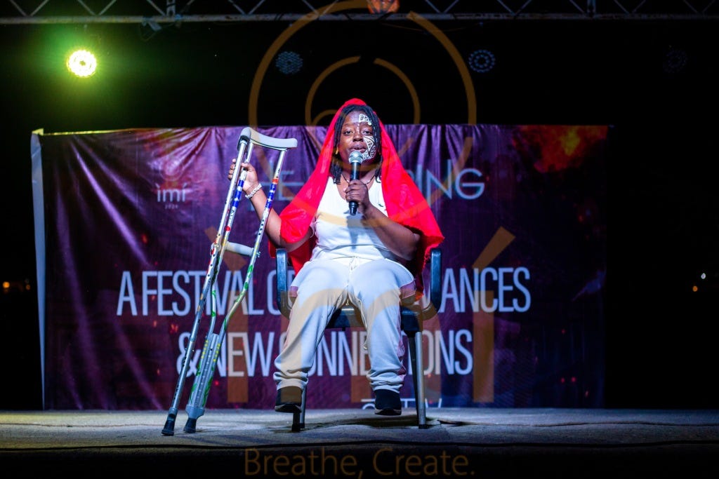 A woman dressed in white, wearing a red scarf performs poetry while holding her crutches.