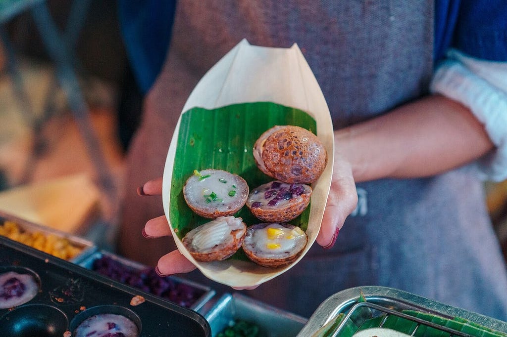 A woman holding an asortment of colorful Thai coconut pancakes
