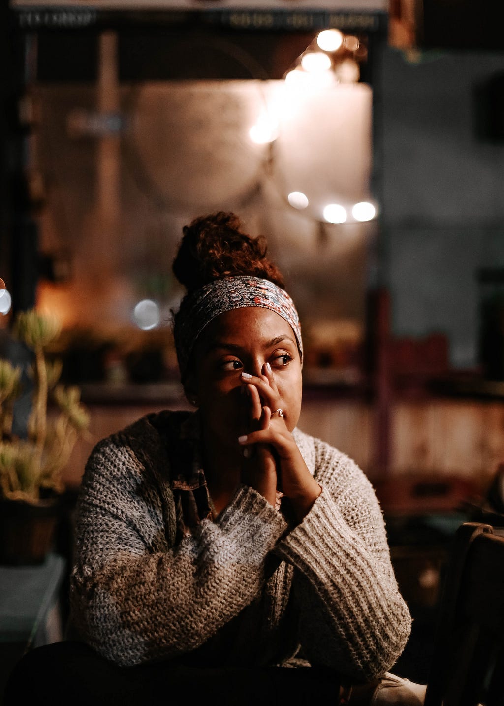 A women sits with her hands clasped in deep thought.