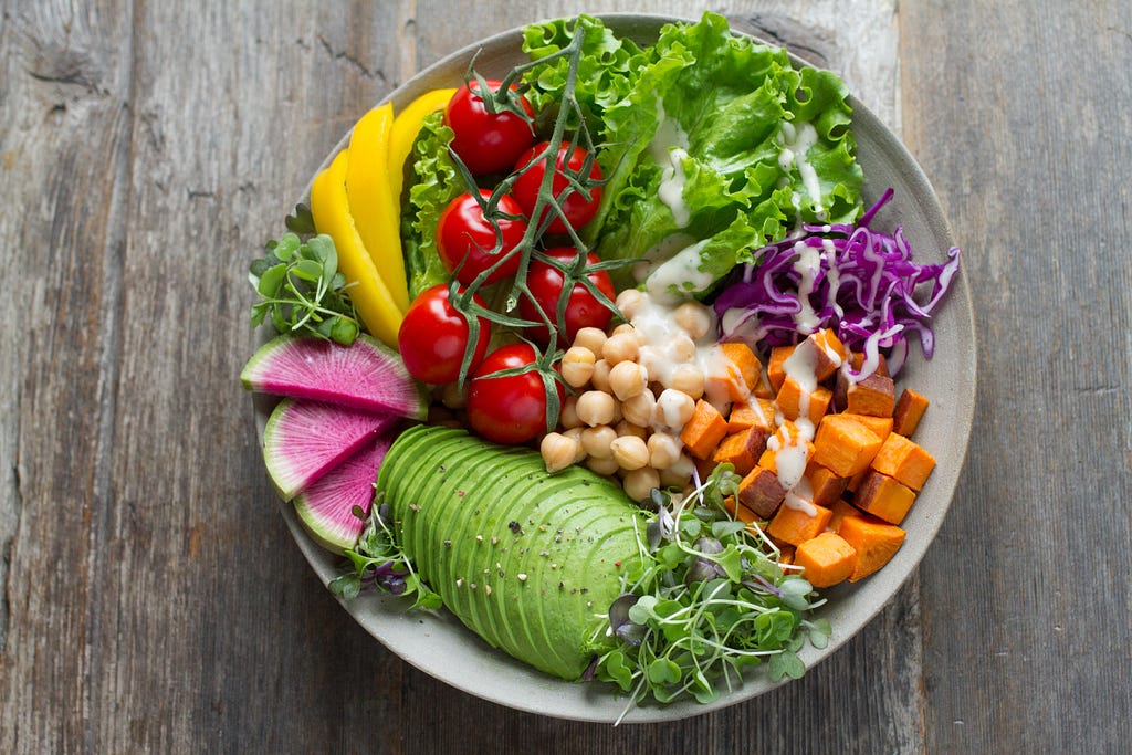 Immagine di un piatto contenente appetitosi ingredienti vegetali tra cui avocado, ceci, pomodorini, insalate di vario tipo, fichi, ecc