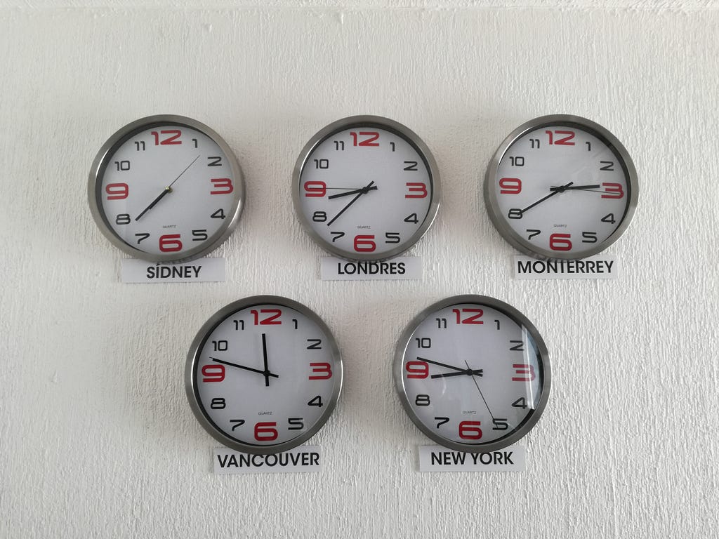 Five clocks hanging on a wall, pointing at different time zones.
