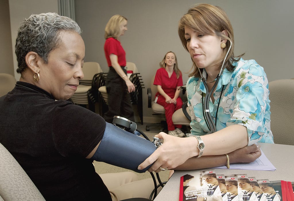 A white woman checking a black woman’s blood pressure