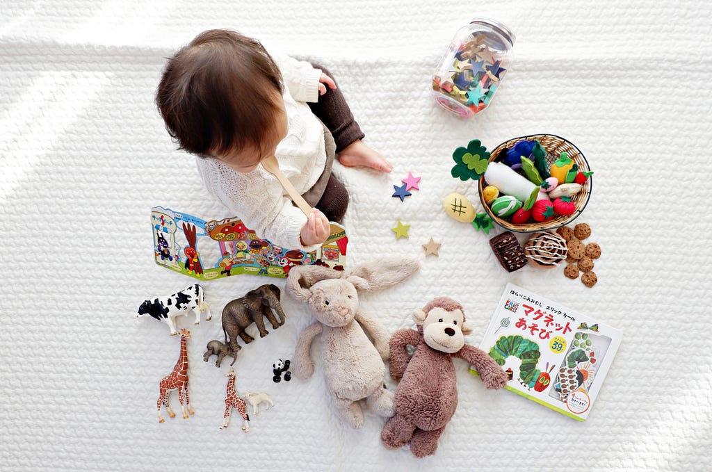 young toddler on white blanket deciding what toy to play with