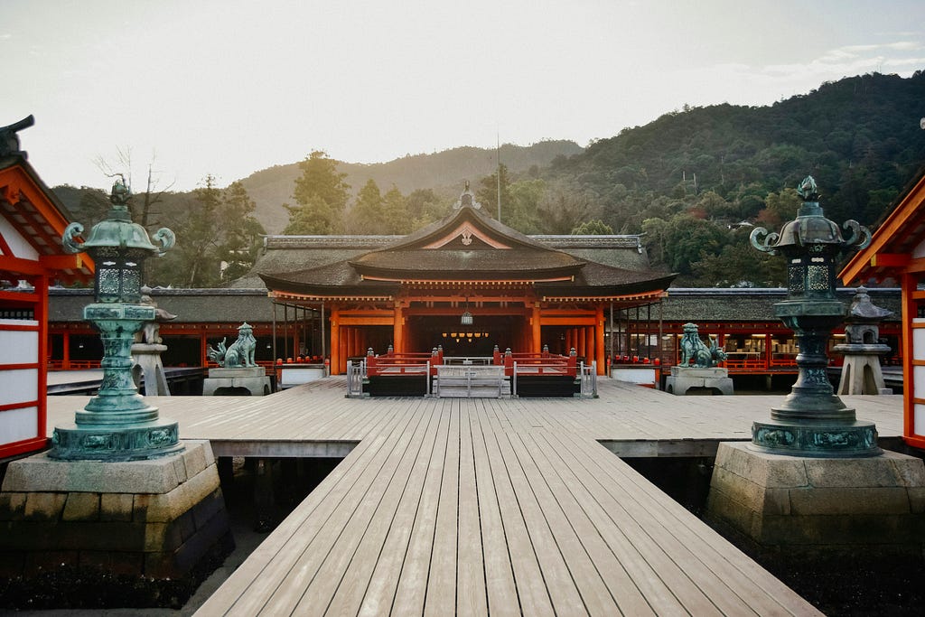 The approach to a large jinja, showing the various buildings, water stations, stone lions, and stone lanterns. All these are arranged symmetrically either side of the wooden platform leading to the main building.