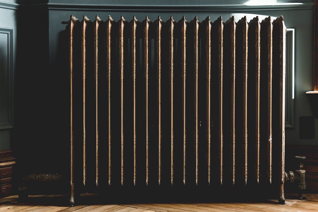 A radiator set against a dark wall, with sunlight shining in